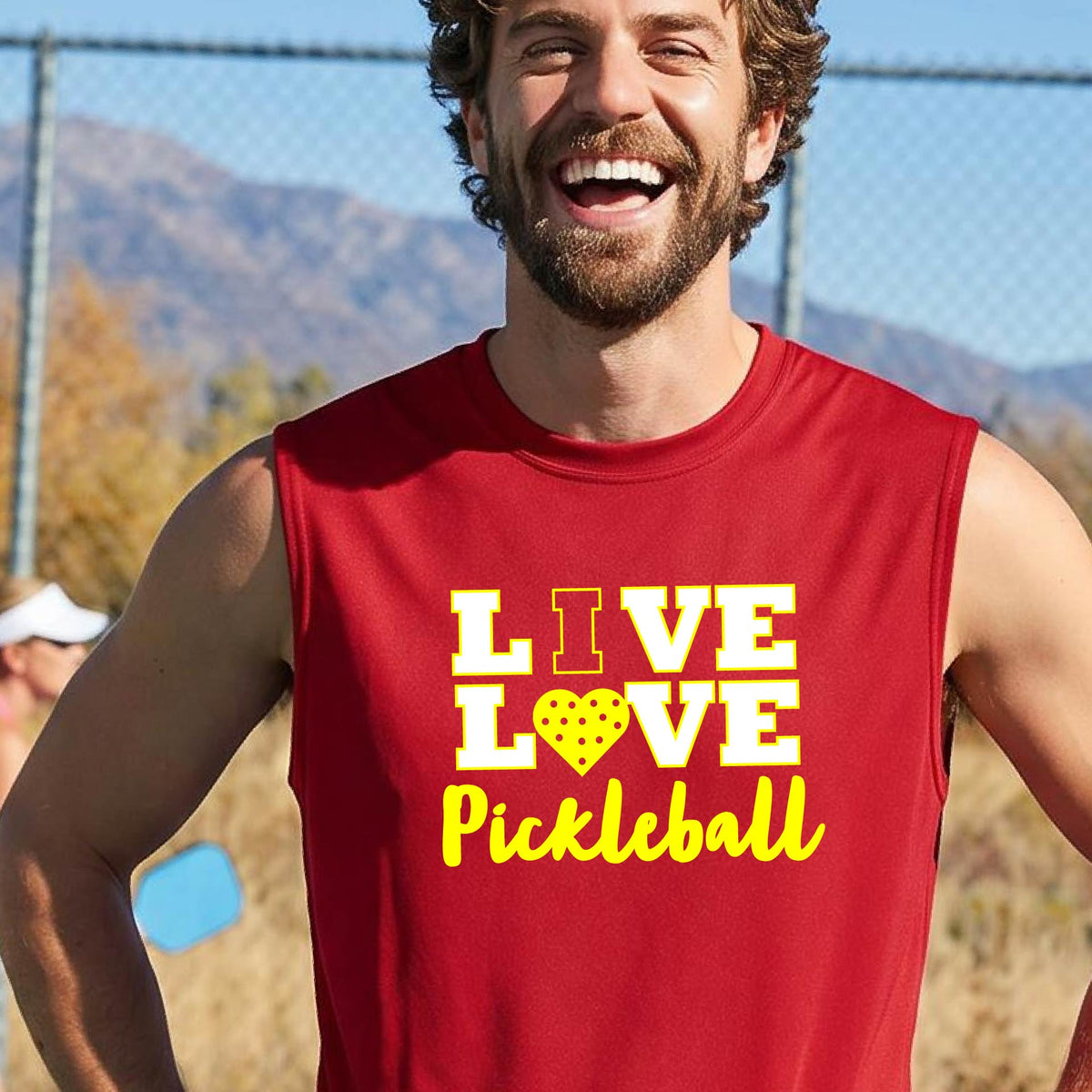A man on a pickleball court wearing a lime red sleeveless V-neck shirt with a yellow graphic that reads 'LIVE LOVE Pickleball' and a heart-shaped pickleball dot pattern inside the word 'LOVE'.