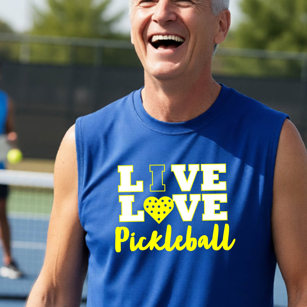 A man on a pickleball court wearing a lime royal blue sleeveless V-neck shirt with a yellow graphic that reads 'LIVE LOVE Pickleball' and a heart-shaped pickleball dot pattern inside the word 'LOVE'.