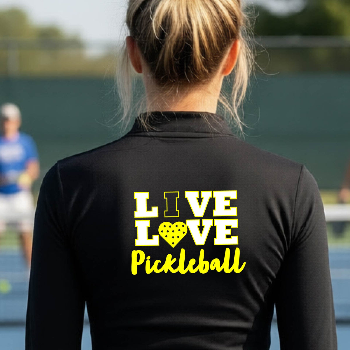 A woman viewed from behind wearing a black quarter-zip athletic pullover with a yellow and white graphic on the back that reads 'LIVE LOVE Pickleball'.