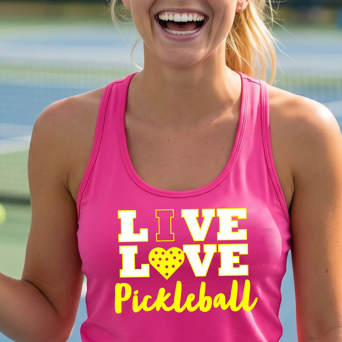 A woman on a pickleball court wearing a pink tank top with a yellow and white graphic that reads 'LIVE LOVE Pickleball' with a heart shaped pickleball motiff replace the O.