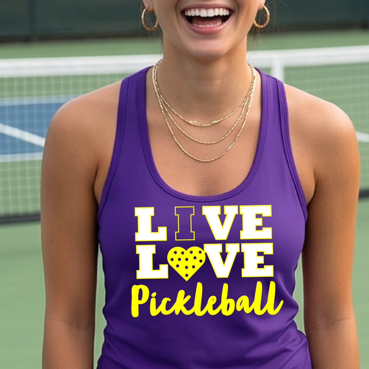 A woman on a pickleball court wearing a purple tank top with a yellow and white graphic that reads 'LIVE LOVE Pickleball' with a heart shaped pickleball motiff replace the O.