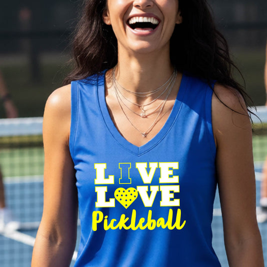 A woman on a pickleball court wearing a bright blue sleeveless tank top with the text 'LIVE LOVE Pickleball' printed in white and yellow. The background shows a blurred pickleball court net and outdoor setting.