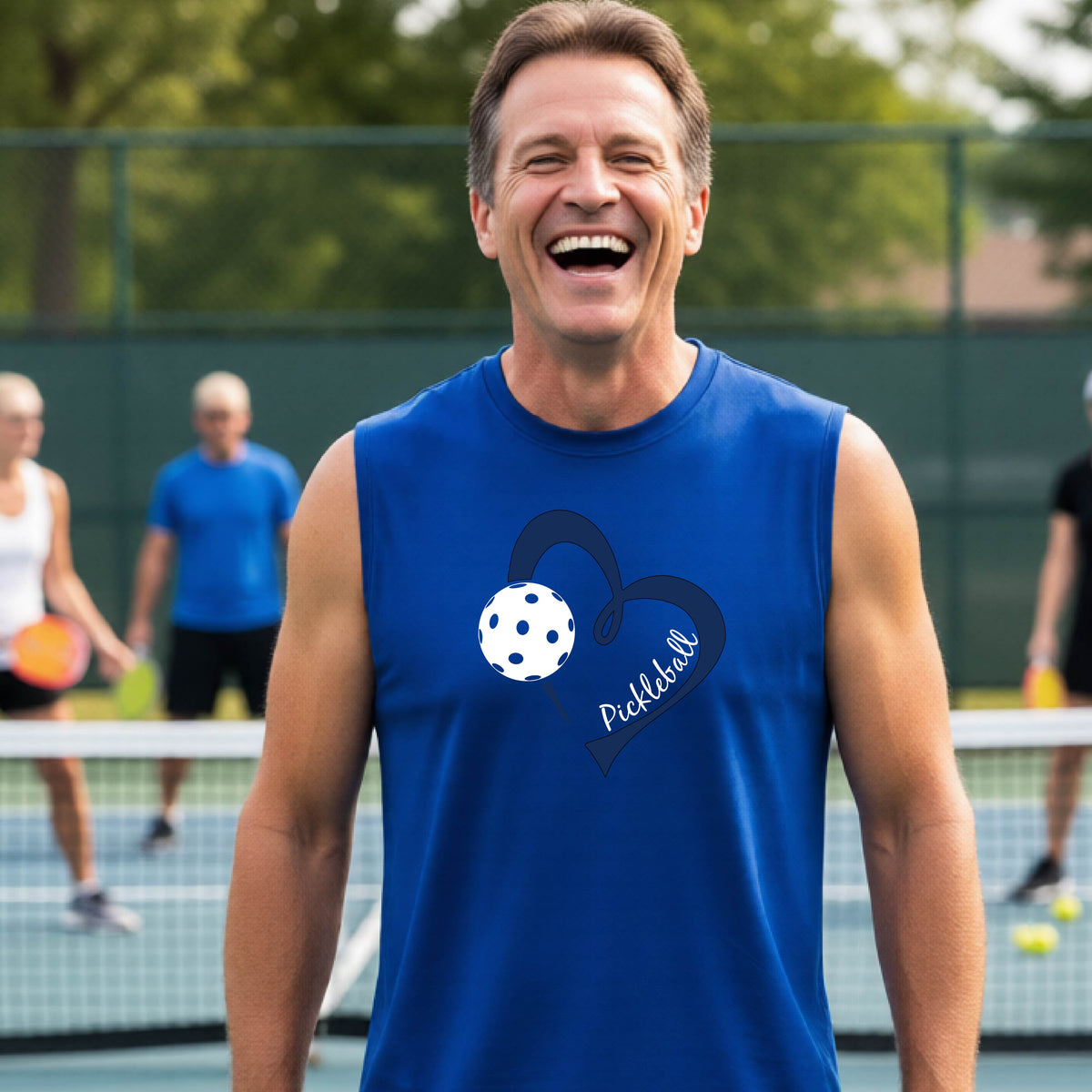 A smiling man on a pickleball court wearing a bright royal blue sleeveless shirt with a navy heart, pickleball graphic, and the word 'Pickleball' printed on the front.