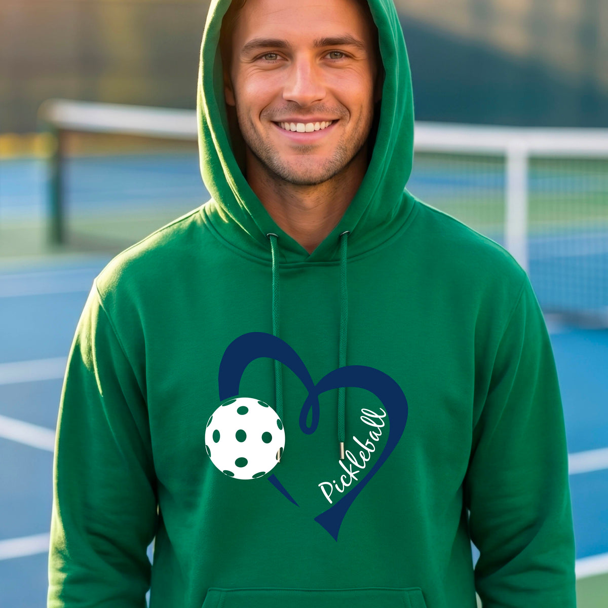 A smiling man wearing a green pullover hoodie with a navy blue heart outline, a white pickleball graphic, and the word 'Pickleball' on the front.