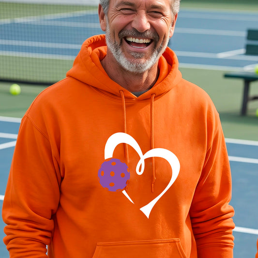 A smiling man wearing an orange hoodie with a white heart outline and a purple pickleball graphic on the front.