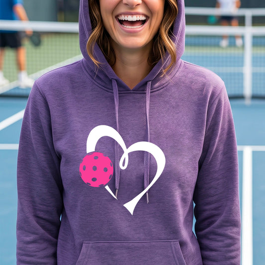 A woman wearing a purple hoodie pullover with a white heart and a pink pickleball graphic on a  blue pickleball court.
