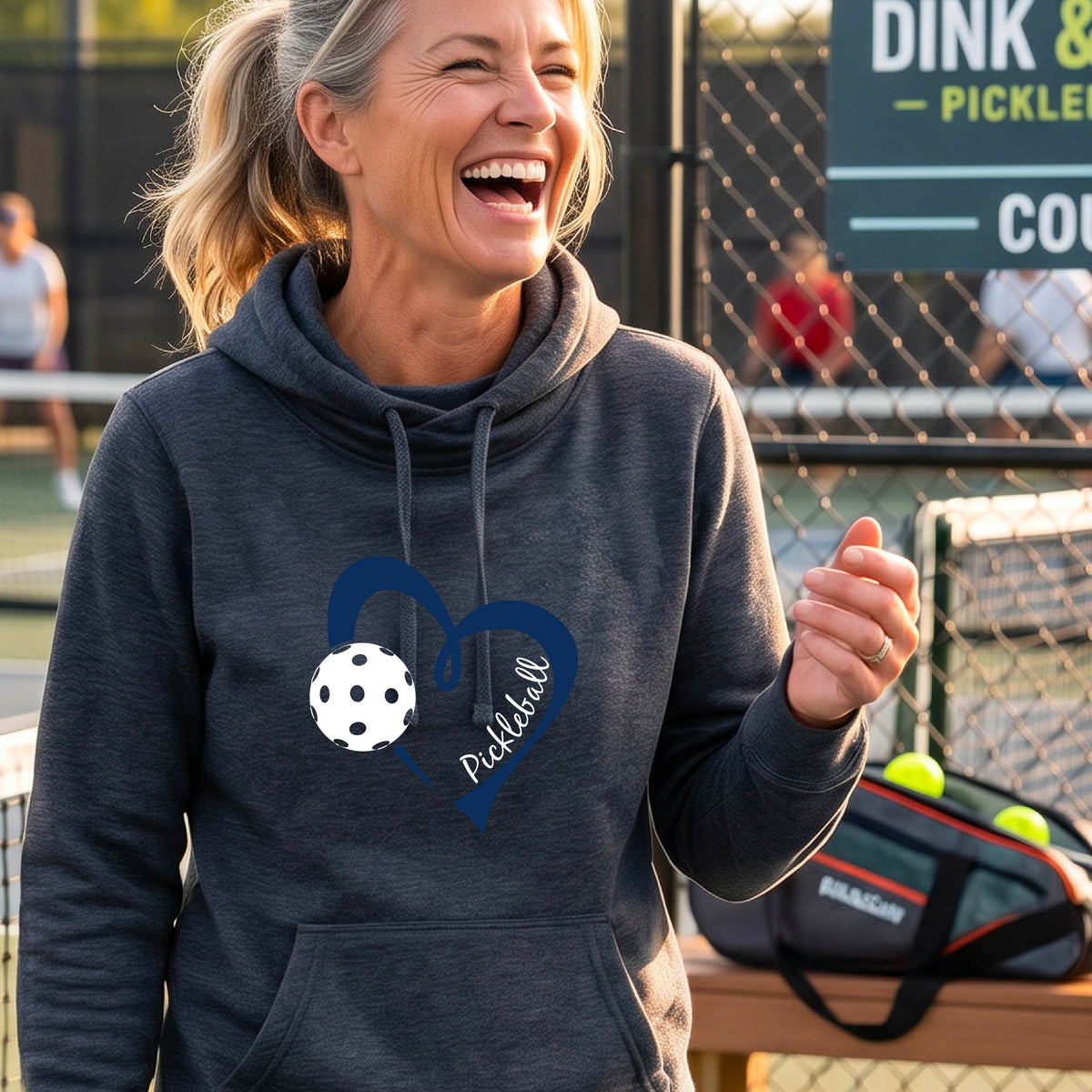 A woman wearing a navy blue cowl-neck hoodie with a navy blue heart outline, a white pickleball graphic, and the word 'Pickleball' printed on the front.