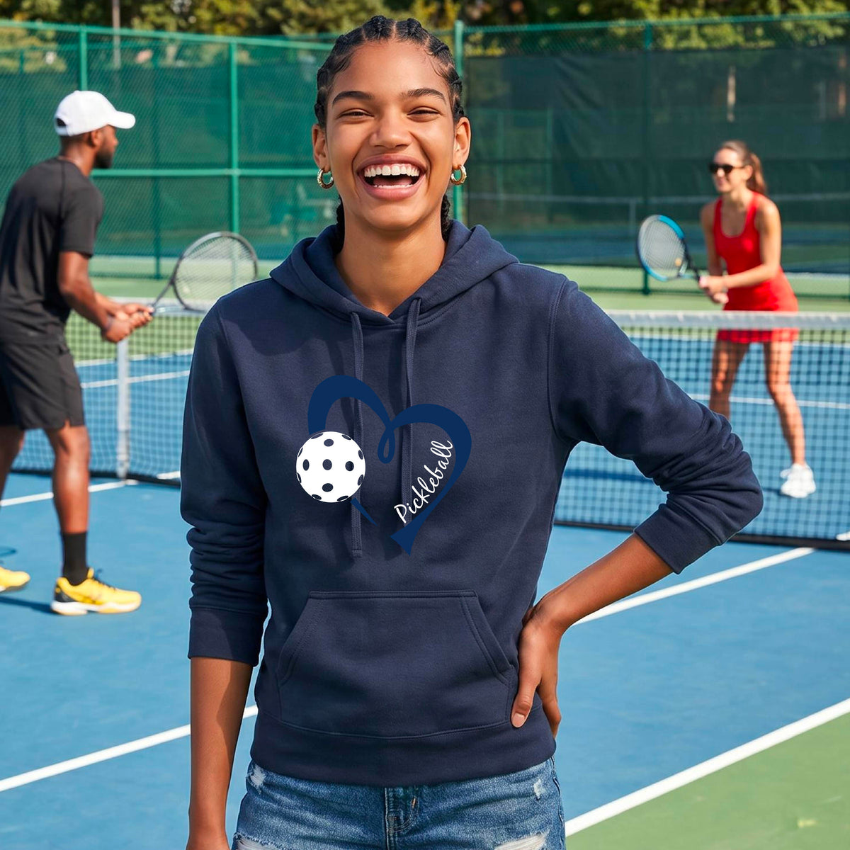 A woman wearing a navy blue pullover hoodie with a navy blue heart outline, a white pickleball, and the word 'Pickleball' printed on the front.