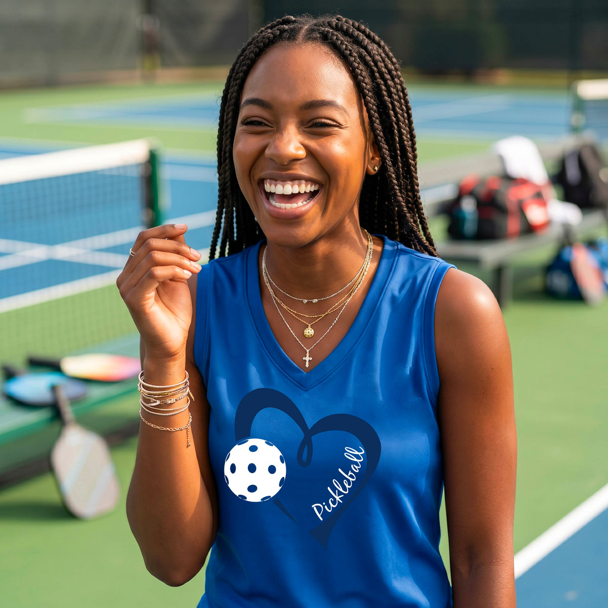 A smiling woman on a pickleball court wearing a royal blue sleeveless tank top with a navy heart outline, a white pickleball graphic, and the word 'Pickleball' printed on the front.