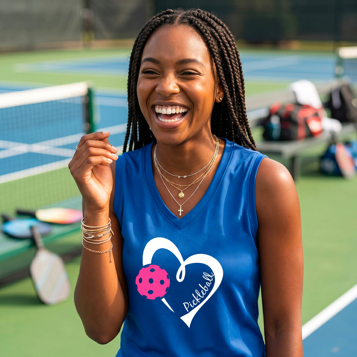 A smiling woman on a pickleball court wearing a royal bluel  sleeveless athletic tank top with a white heart outline, pink pickleball graphic, and the word 'Pickleball' printed on the front.