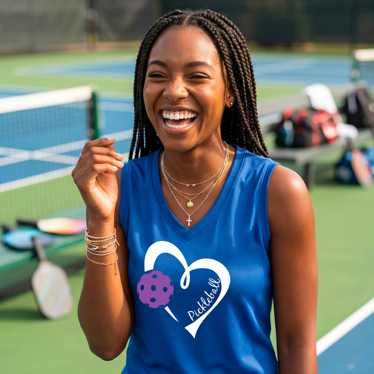 A woman smiling on a pickleball court wearing a royal blue sleeveless tank top with a white heart outline, a purple pickleball graphic, and the word 'Pickleball' printed on the front.