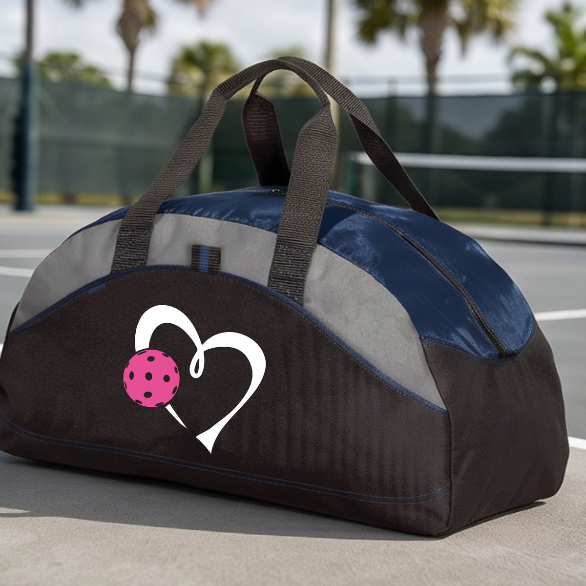 A black and navy blue pickleball duffel bag with gray panels, featuring a white heart outline and a pink pickleball graphic on the front,.