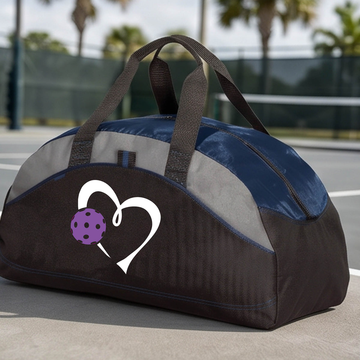 A black and navy blue pickleball duffel bag with gray panels, featuring a white heart outline and a purple pickleball graphic on the front,.