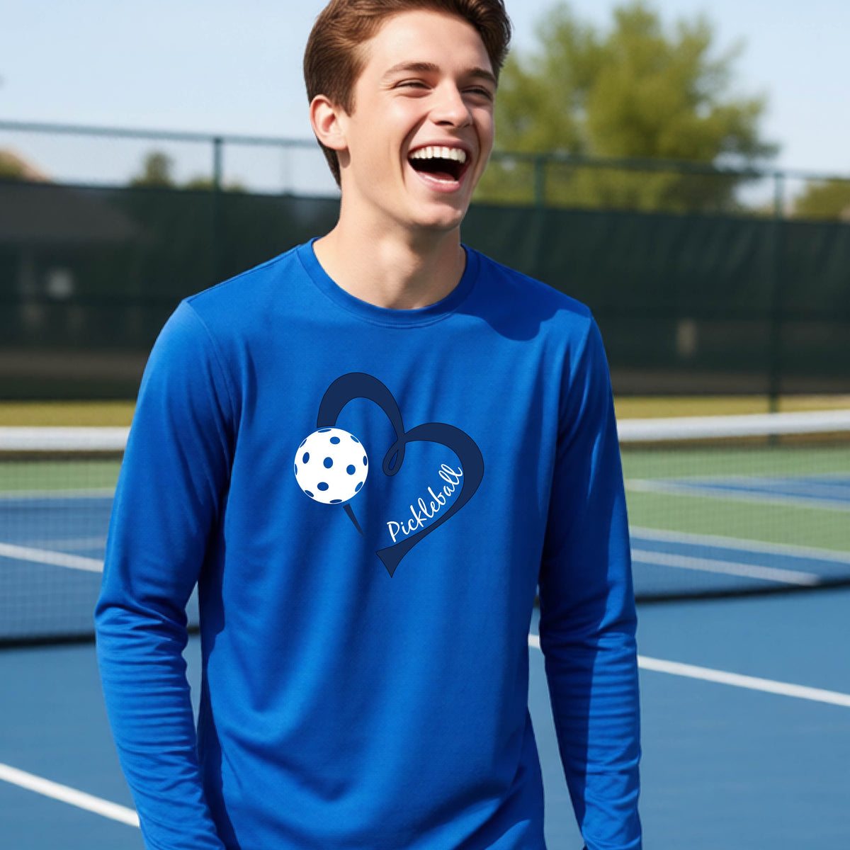 A young person wearing a royal blue long-sleeve athletic t-shirt with a navy blue heart, a white pickleball, and the text 'Pickleball' in script on the front of the shirt. 