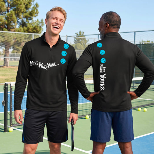 Two men on a pickleball court wearing matching black quarter-zip pullover shirts. One shows the front with the text 'MINE MINE MINE' along with three pickleball graphics. and the back text 'JUST KIDDING YOURS, along with three pickleball graphics.