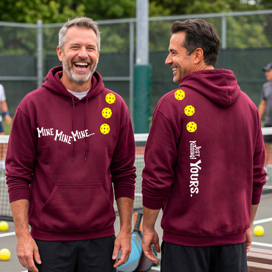 Two men on a pickleball court wearing matching maroon unisex hoodie pullovers. One shows the front with the text 'MINE MINE MINE' along with three pickleball graphics. and the back text 'JUST KIDDING YOURS, along with three pickleball graphics.