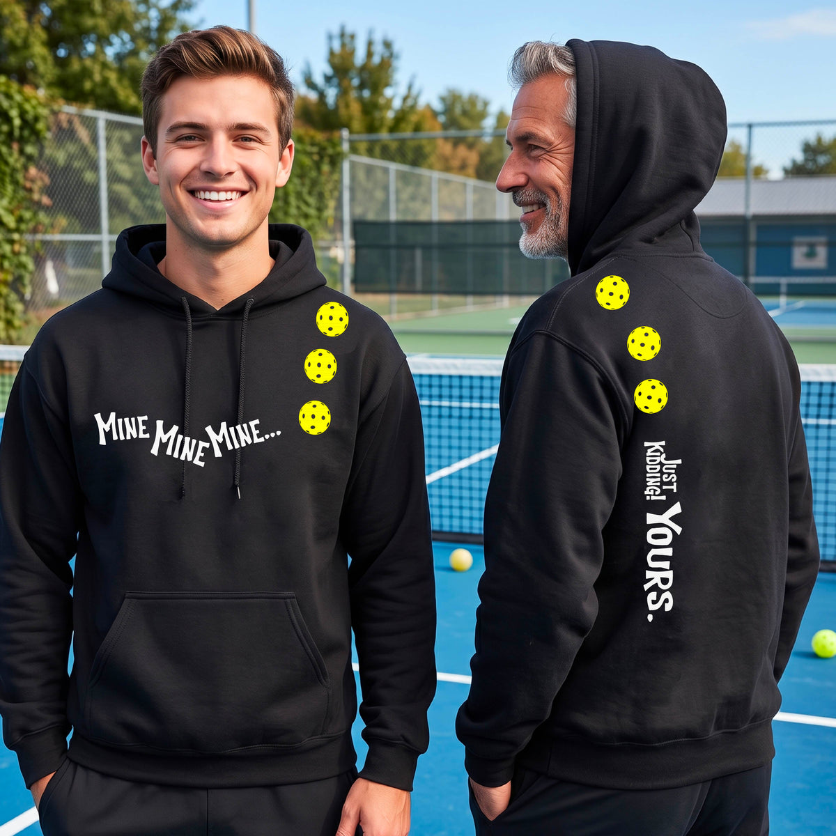 Two men on a pickleball court wearing matching black unisex hoodie pullovers. One shows the front with the text 'MINE MINE MINE' along with three pickleball graphics. and the back text 'JUST KIDDING YOURS, along with three pickleball graphics.