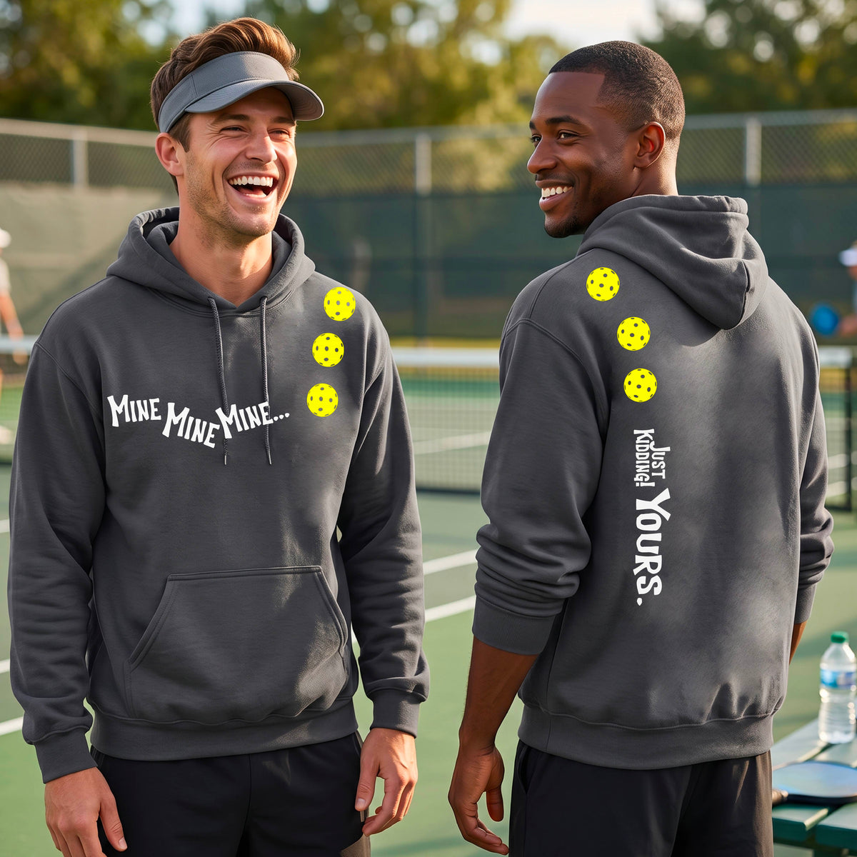 Two men on a pickleball court wearing matching gray unisex hoodie pullovers. One shows the front with the text 'MINE MINE MINE' along with three pickleball graphics. and the back text 'JUST KIDDING YOURS, along with three pickleball graphics.