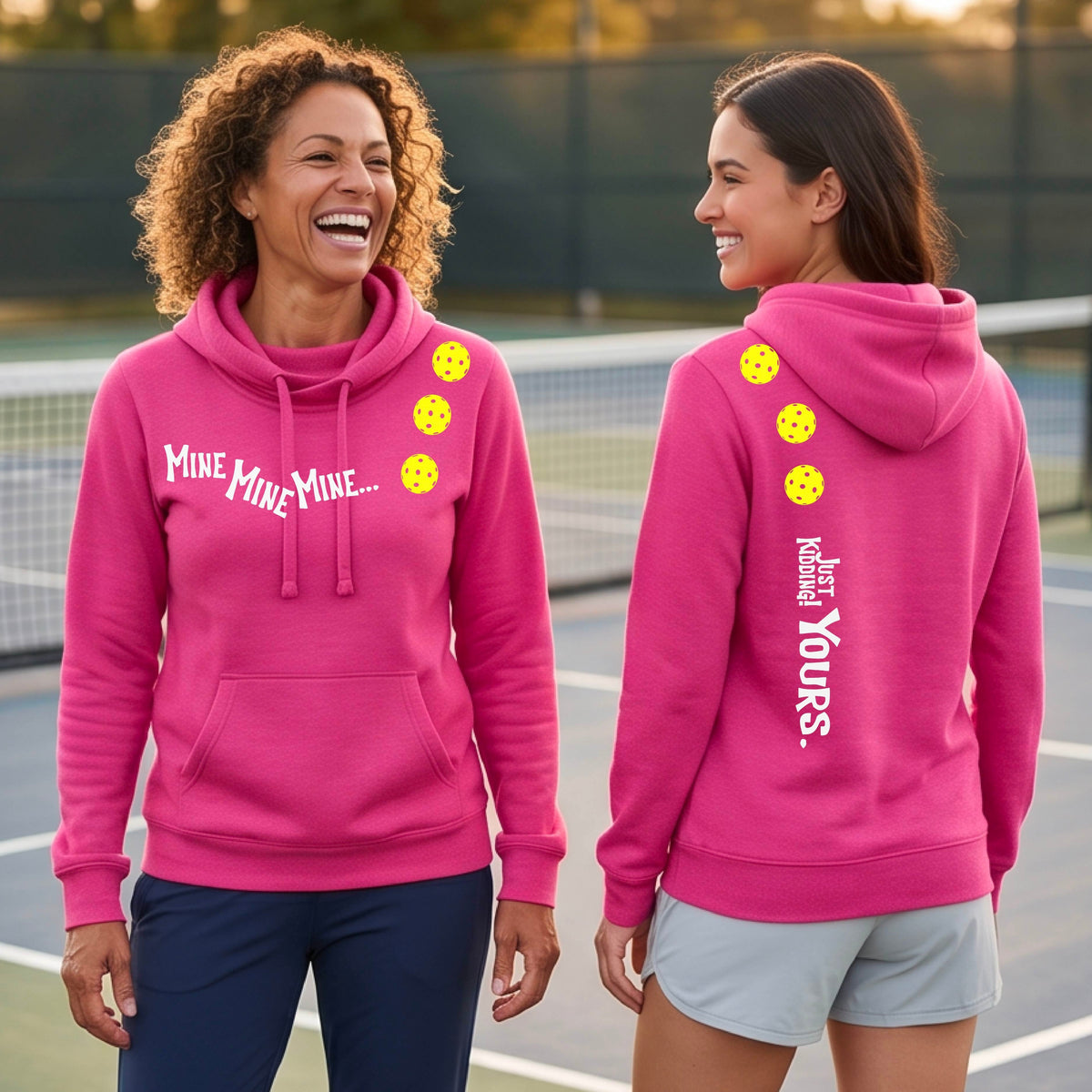 Two women on a pickleball court wearing matching cowl-neck pink hoodies One shows the front with the text 'MINE MINE MINE' along with three pickleball graphics. and the back text 'JUST KIDDING YOURS, along with three pickleball graphics.