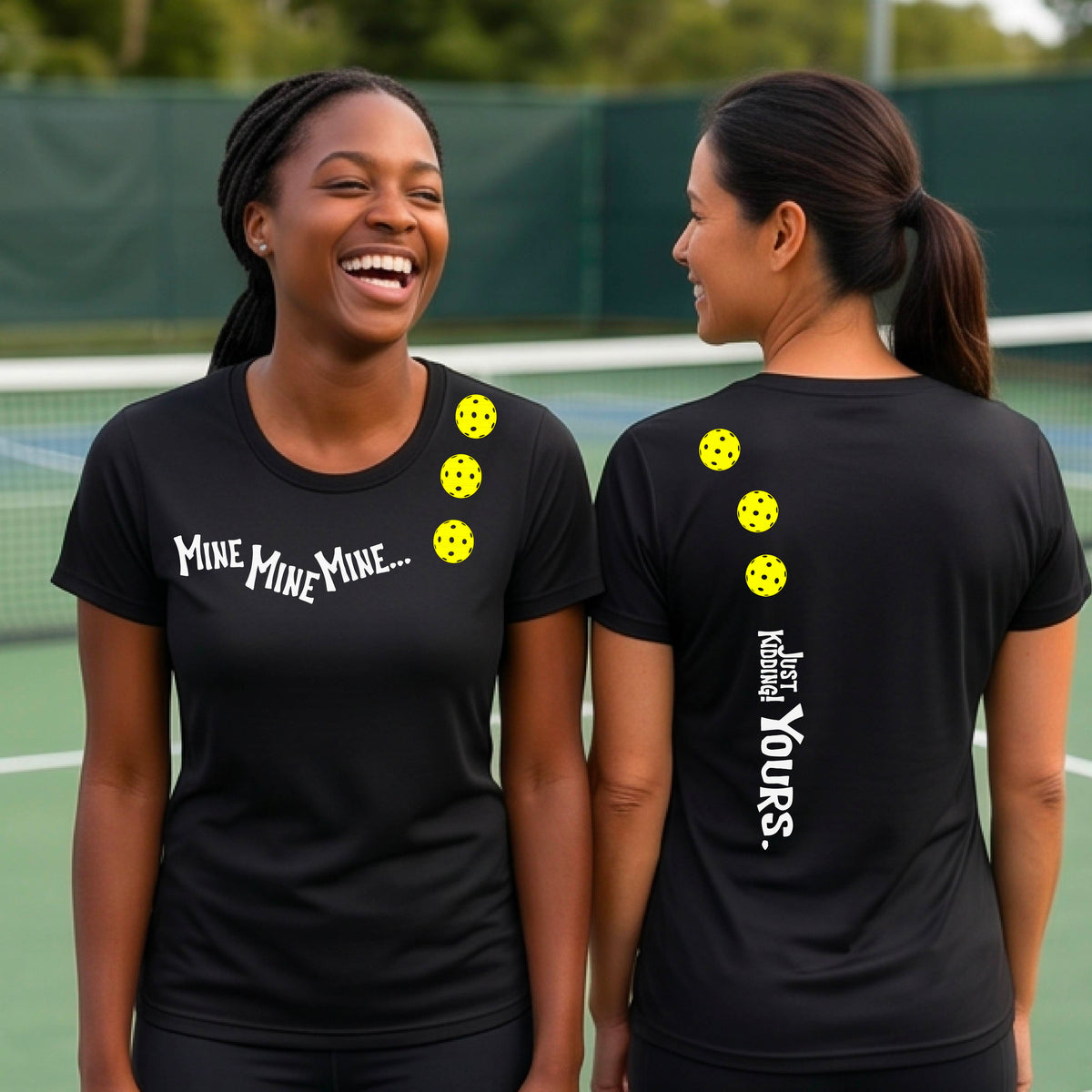 Two women on a pickleball court wearing matching black short-sleeve atghletic t-shirts. One shows the front with the text 'MINE MINE MINE' along with three pickleball graphics. and the back text 'JUST KIDDING YOURS, along with three pickleball graphics.