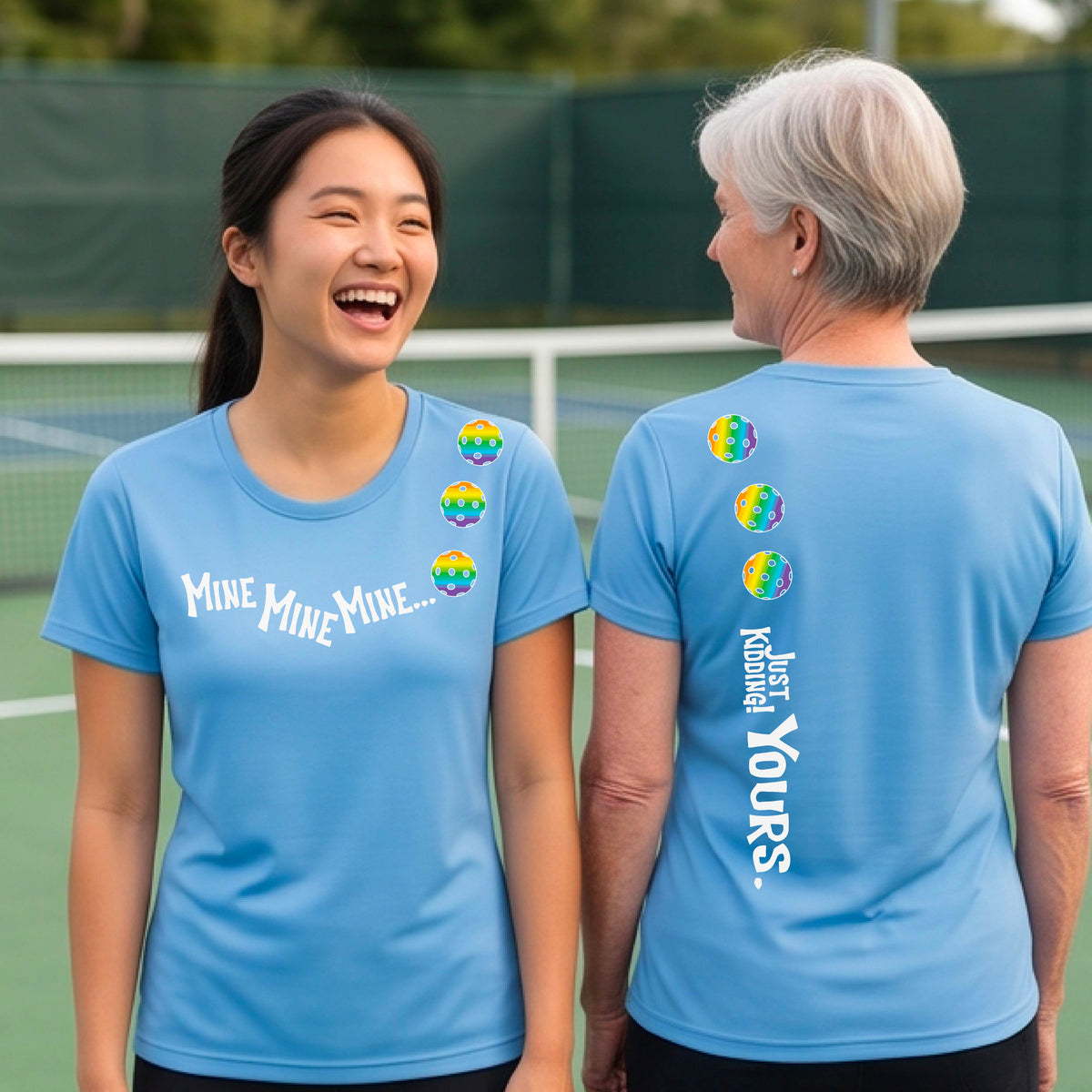 Two women on a pickleball court wearing matching blue short-sleeve atghletic t-shirts. One shows the front with the text 'MINE MINE MINE' along with three pickleball graphics. and the back text 'JUST KIDDING YOURS, along with three pickleball graphics.