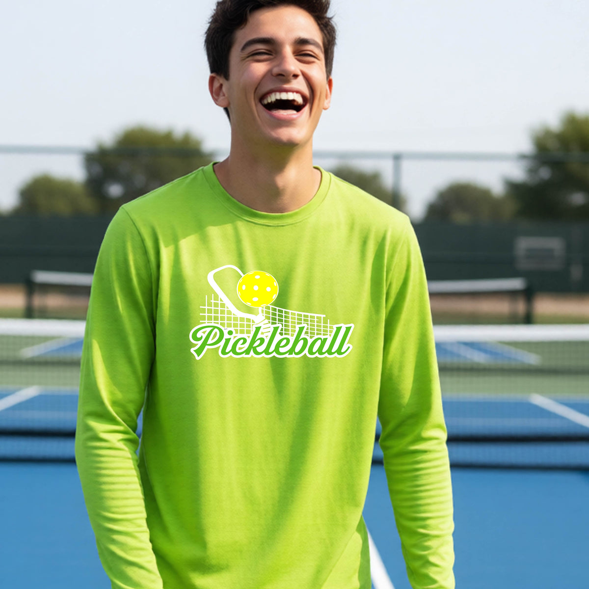 A young person wearing a lime green long sleeve t-shirt with a graphic that has white and green text "PICKLEBALL'  with a white pickleball paddle and net and a yellow pickleball above the text.