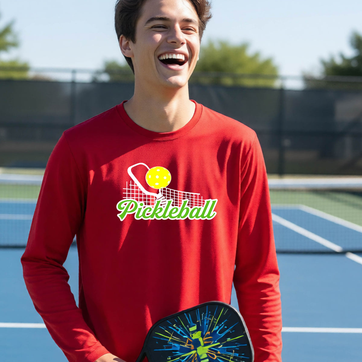A young person wearing a red long sleeve t-shirt with a graphic that has white and green text "PICKLEBALL'  with a white pickleball paddle and net and a yellow pickleball above the text.
