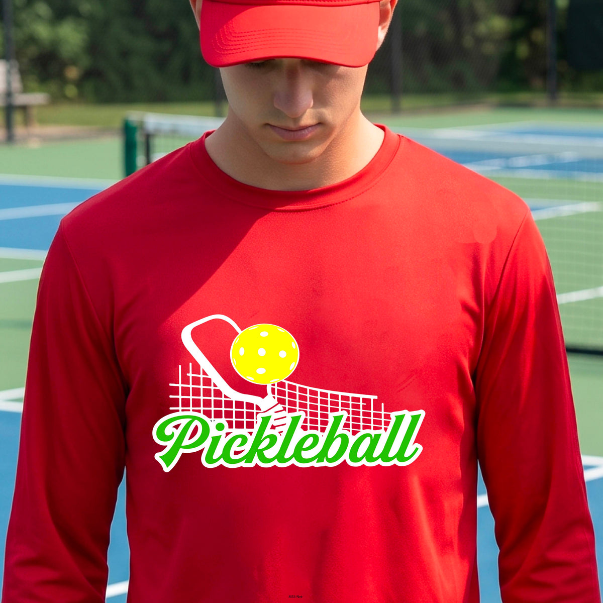 A woman wearing a red long-sleeve t-shirt with a graphic on the front that has white and green text "PICKLEBALL'  with a white pickleball paddle and net and a yellow pickleball above the text graphic.
