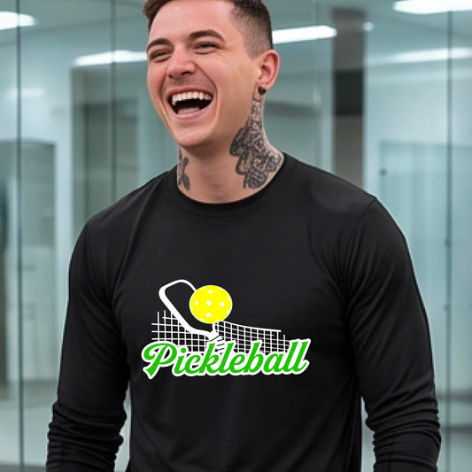 A woman wearing a black long-sleeve t-shirt with a graphic on the front that has white and green text "PICKLEBALL'  with a white pickleball paddle and net and a yellow pickleball above the text graphic.