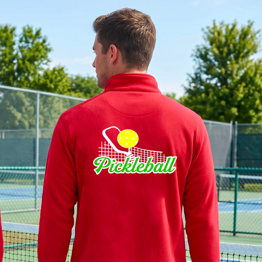 A close-up of a man wearing a red ong-sleeve quarter-zip shirt with a graphic on the front that has white and green text "PICKLEBALL'  with a white pickleball paddle and net and a yellow pickleball above the text graphic.