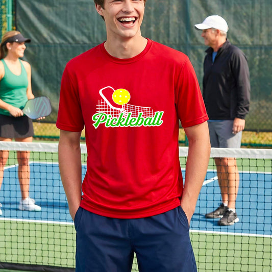 A man wearing a red short-sleeve t-shirt with a graphic on the front that has white and green text "PICKLEBALL'  with a white pickleball paddle and net and a yellow pickleball above the text graphic.