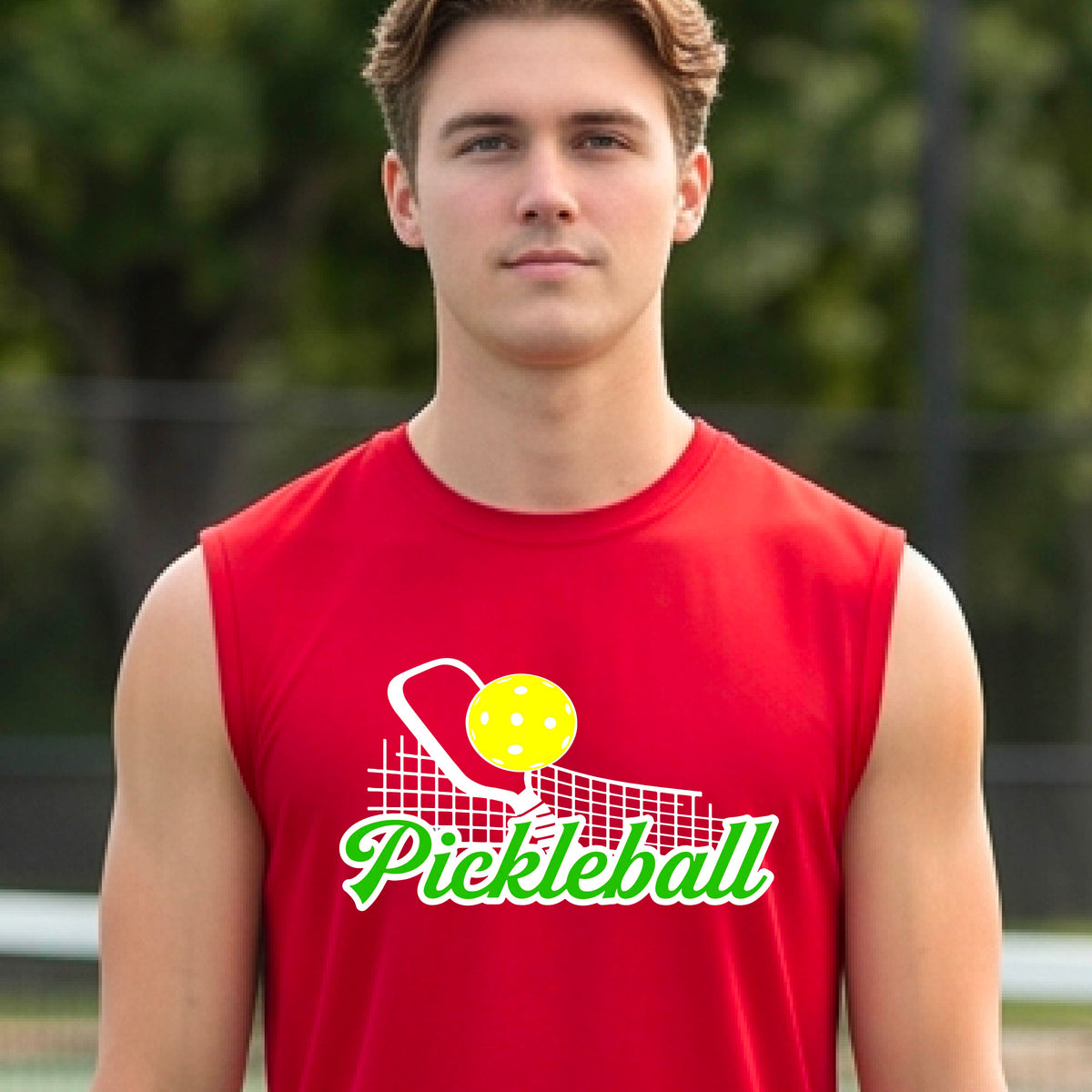 A man wearing a red sleeveless t-shirt with a graphic on the front that has white and green text "PICKLEBALL'  with a white pickleball paddle and net and a yellow pickleball above the text graphic.