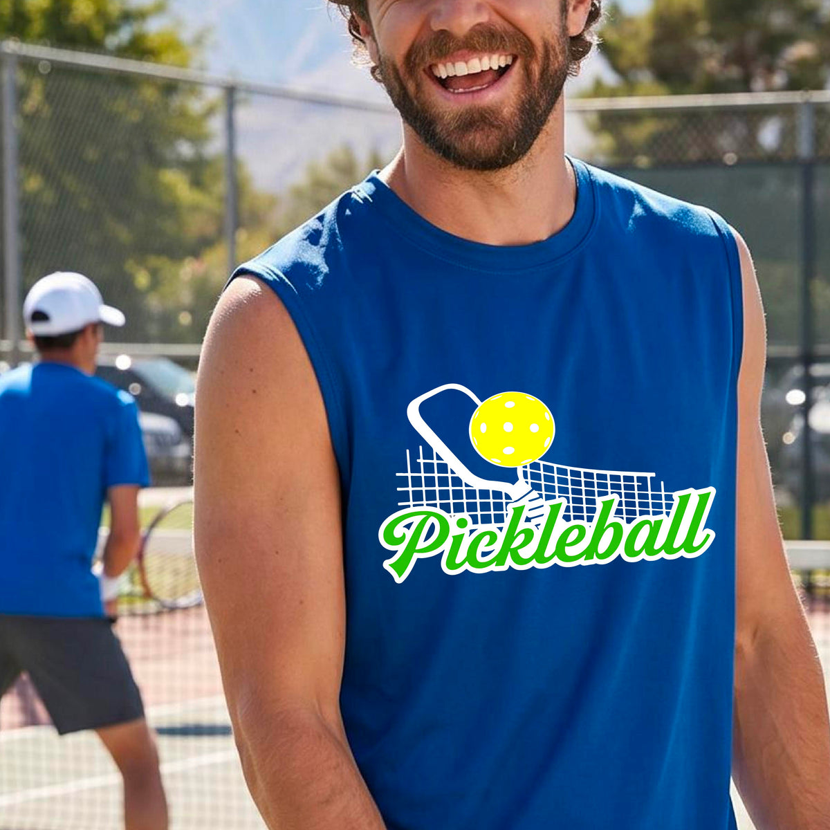 A man wearing a royal blue sleeveless t-shirt with a graphic on the front that has white and green text "PICKLEBALL'  with a white pickleball paddle and net and a yellow pickleball above the text graphic.