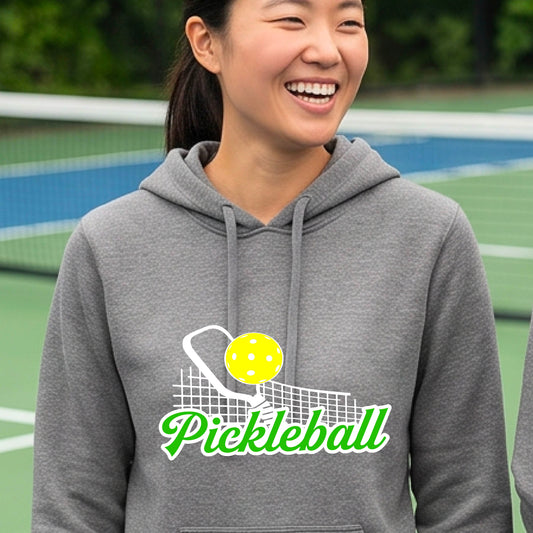 A close-up of a woman wearing a gray long-sleeve fitted hoodie pullover with a graphic on the front that has white and green text "PICKLEBALL'  with a white pickleball paddle and net and a yellow pickleball above the text graphic.