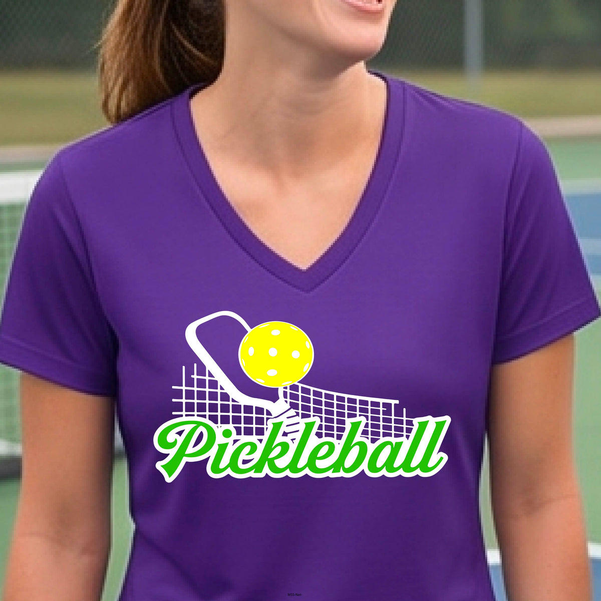 A woman wearing a purple short-sleeve v-neck t-shirt with a graphic on the front that has white and green text "PICKLEBALL'  with a white pickleball paddle and net and a yellow pickleball above the text graphic.