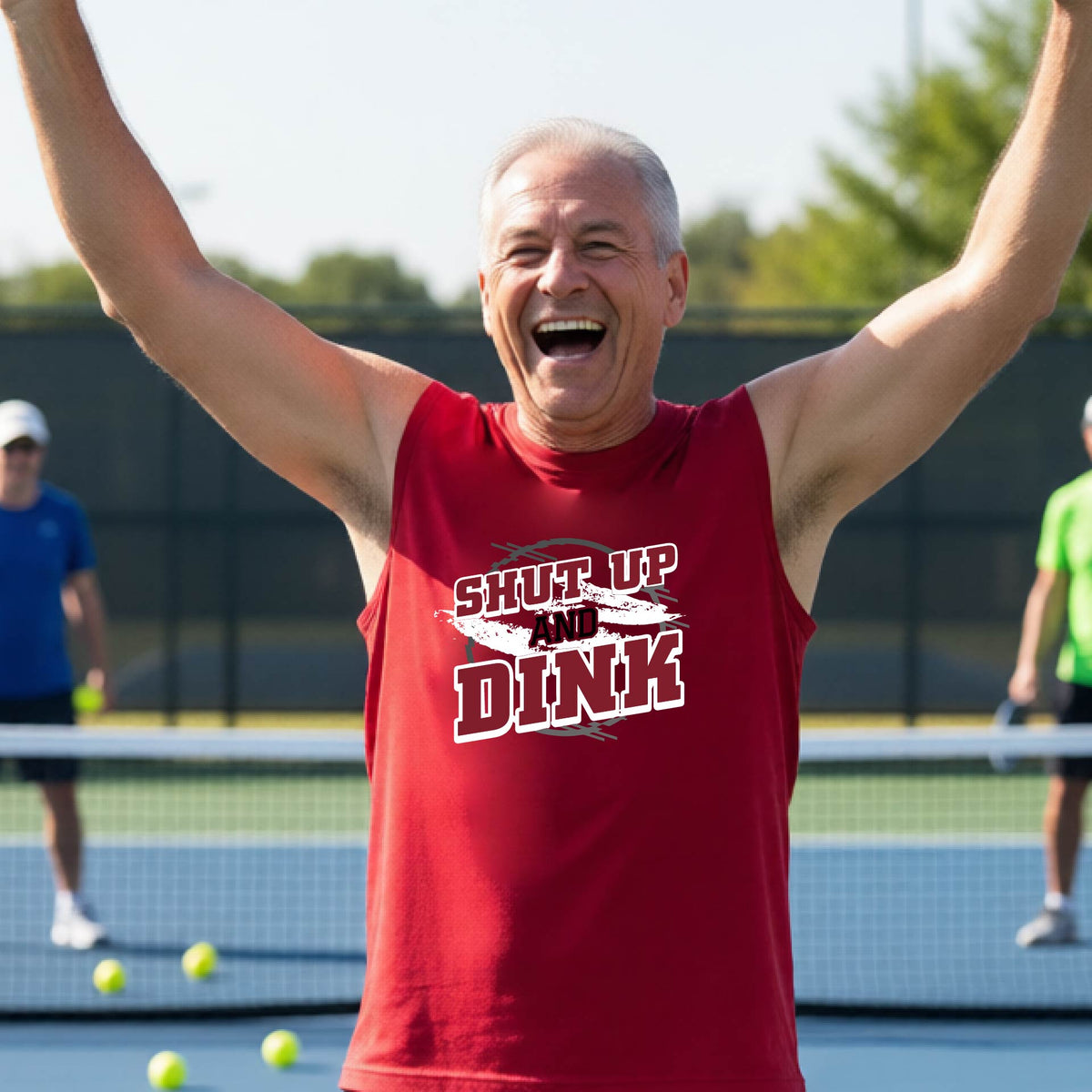 A man on a pickleball court wearing a red sleeveless t-shirt with a white, gray and black graphic of the text: ‘Shut Up and Dink, standing on a pickleball court.