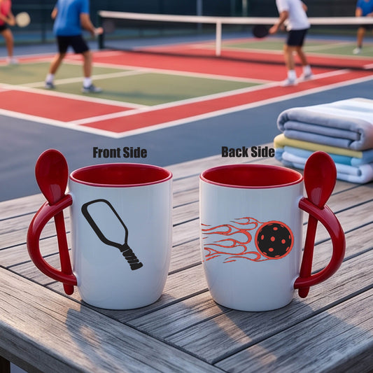 a white and red 12 ounce coffee mug with a built in spoon in the handle with and a fun coffee cup pickleball graphic of a pickleball paddle and a pickleball in motion with fire tail.