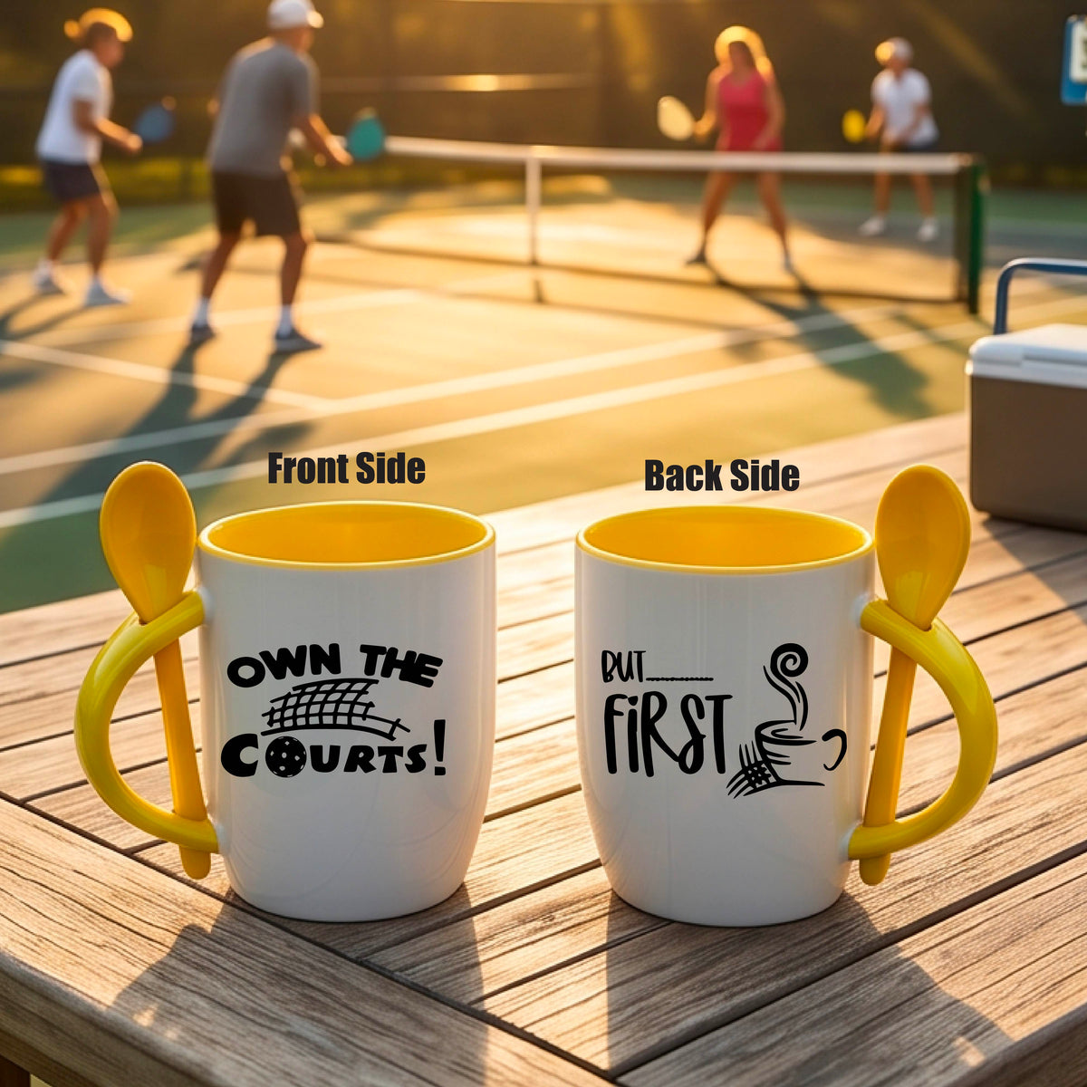 a white and yellow 12 ounce coffee mug with a built in spoon in the handle with and a fun coffee cup and pickleball net graphic and wraparound text 'OWN THE COURTS BUT FIRST PICKLEBALL" 