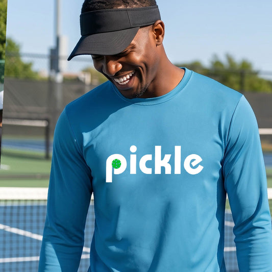 A man wearing a blue long-sleeve t-shirt with a white graphic of ‘PICKLE’ with a green pickleball integrated into the letter P printed on the front, in front of a pickleball court. 