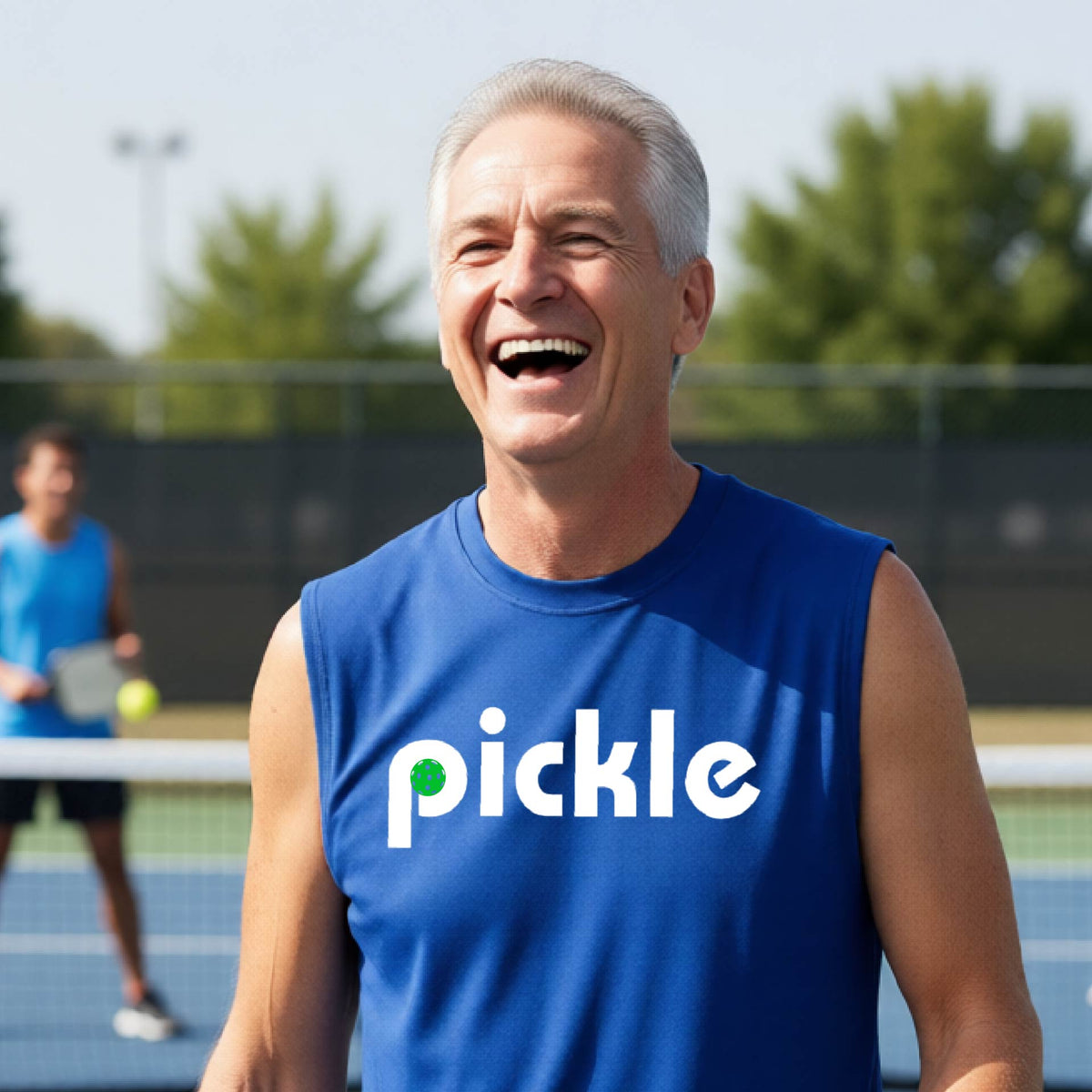 A man wearing a royal blue sleeveless t-shirt with a white graphic of ‘PICKLE’ with a green pickleball integrated into the letter P printed on the front, in front of a pickleball court. 