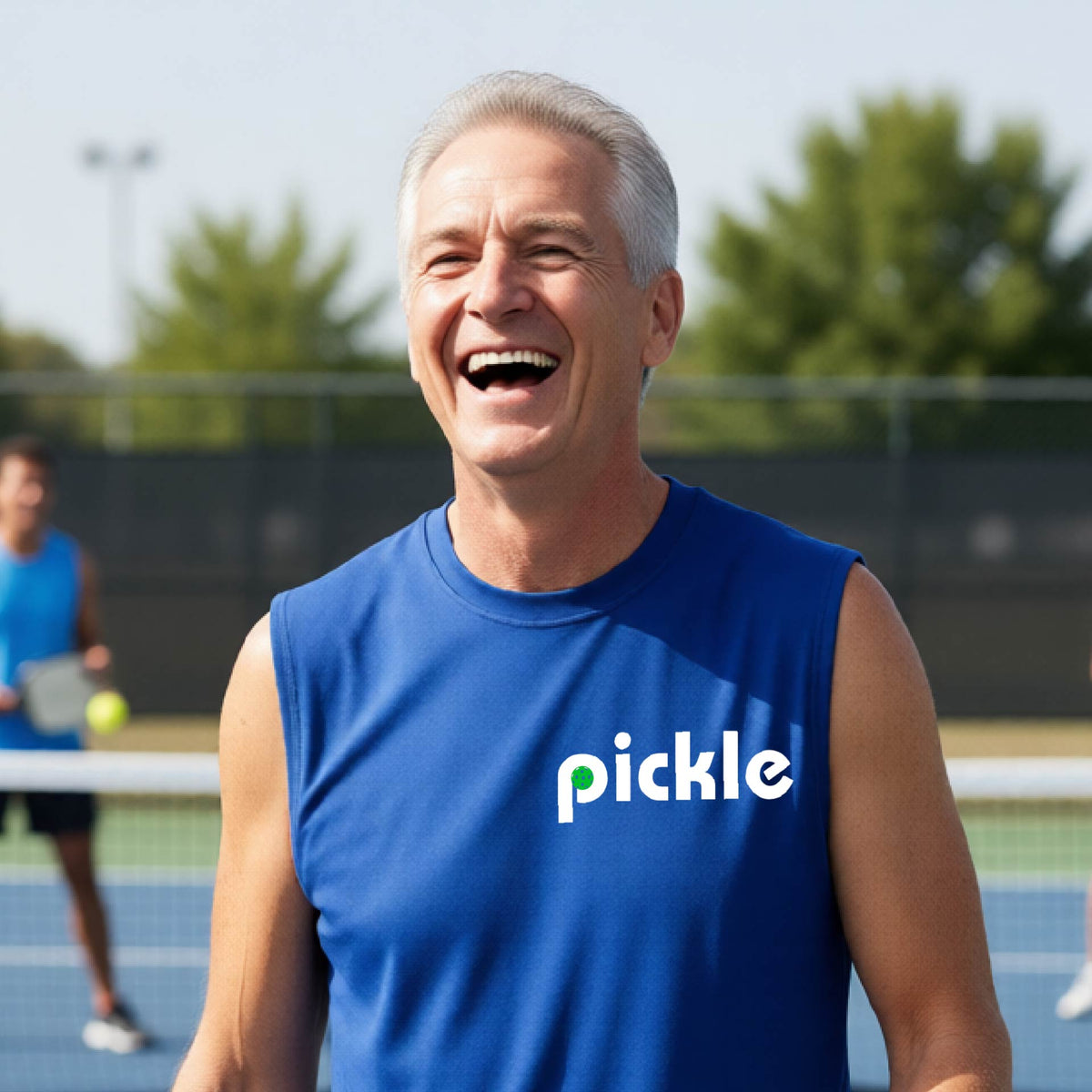 A man wearing a royal blue sleeveless t-shirt with a white graphic of ‘PICKLE’ with a green pickleball integrated into the letter P printed on the front, in front of a pickleball court. 