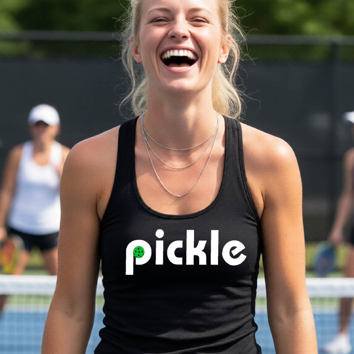 A woman laughing on a pickelball court wearing a black athletic tank top with the word 'pickle' and a green pickelball icon inside the letter P, printed in white across the chest.