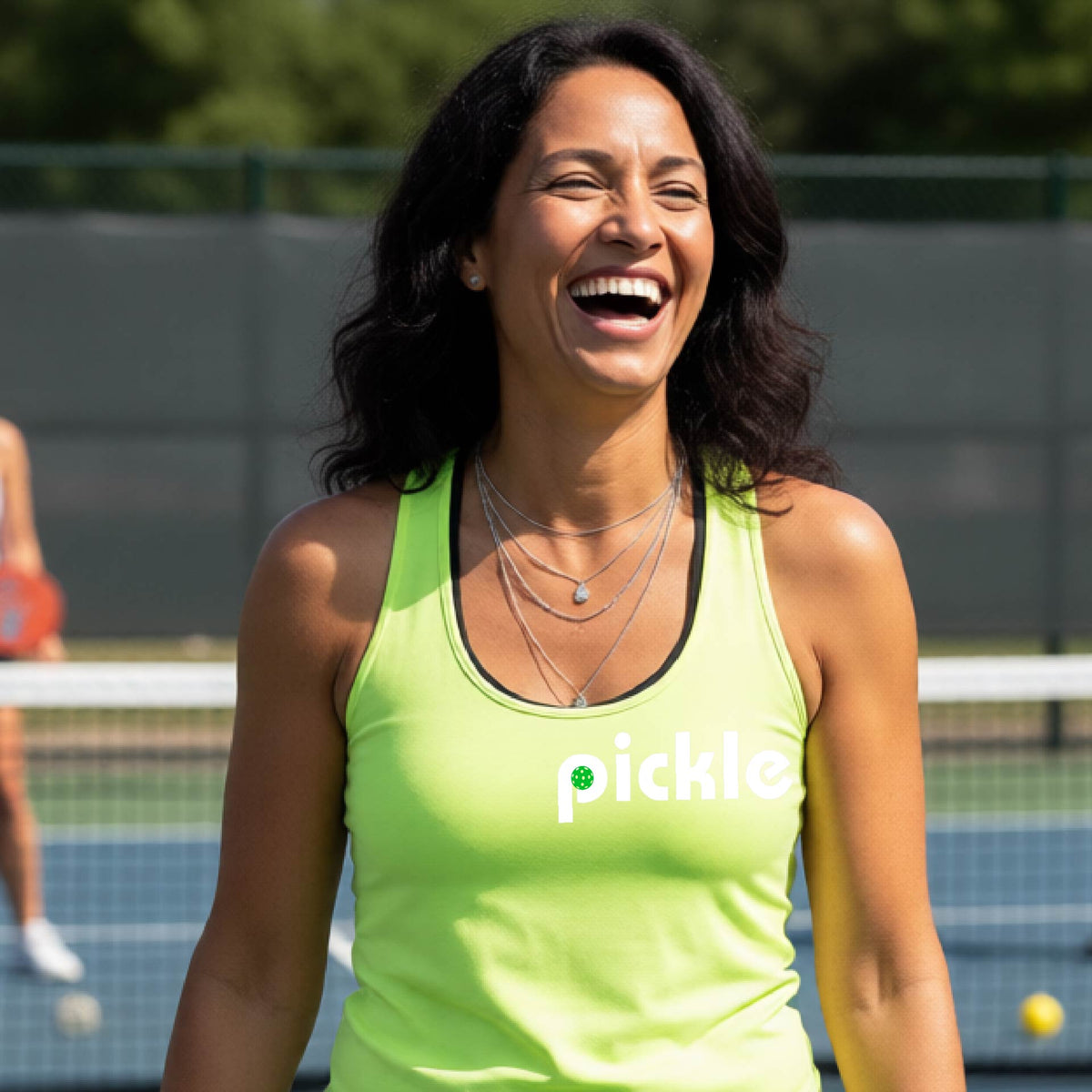 A woman laughing on a pickelball court wearing a lime green athletic tank top with the word 'pickle' and a green pickelball icon inside the letter P, printed in white across the chest.