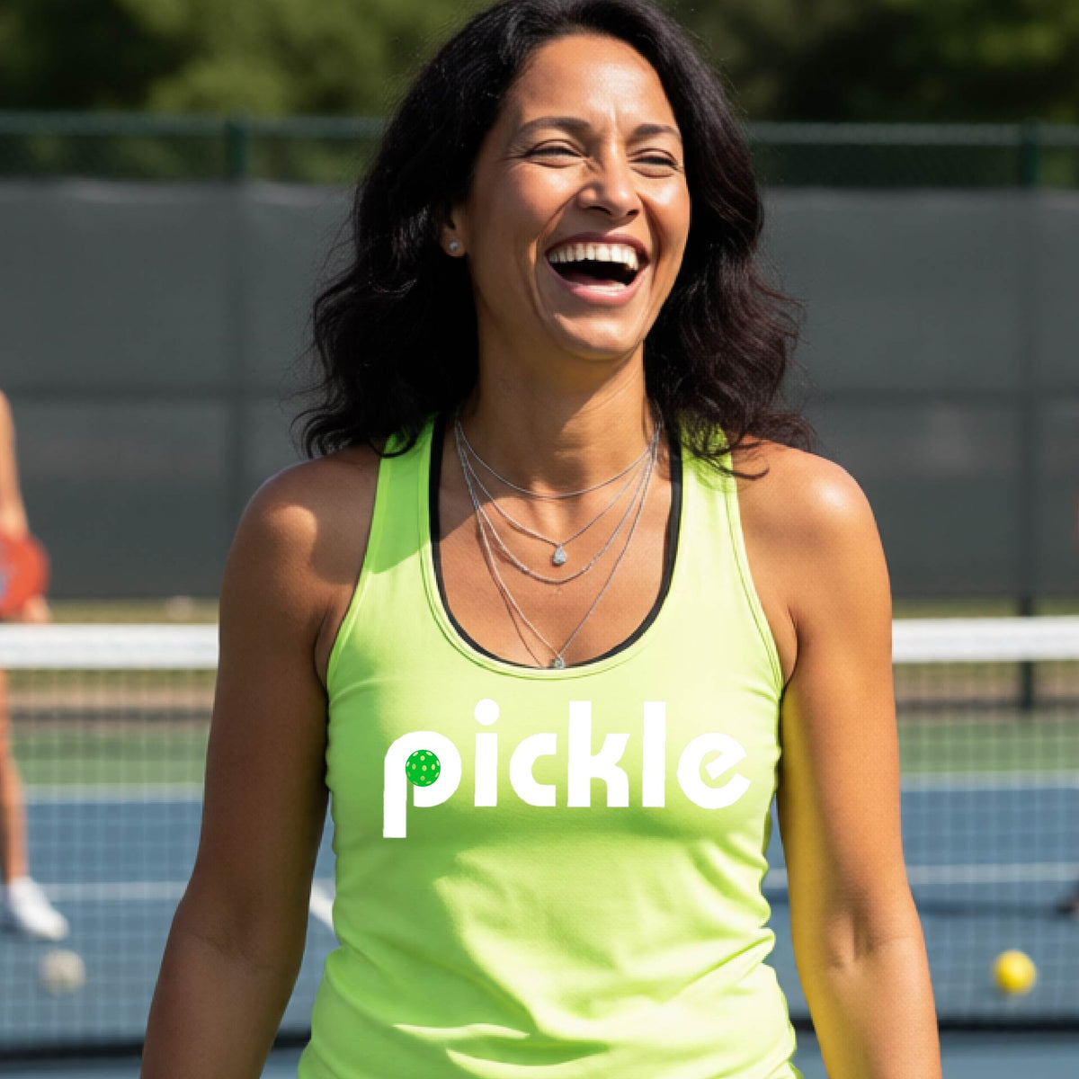 A woman laughing on a pickelball court wearing a lime green athletic tank top with the word 'pickle' and a green pickelball icon inside the letter P, printed in white across the chest.