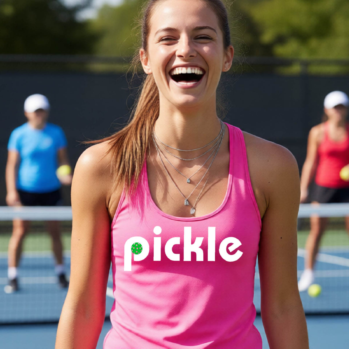 A woman laughing on a pickelball court wearing a pink athletic tank top with the word 'pickle' and a green pickelball icon inside the letter P, printed in white across the chest.