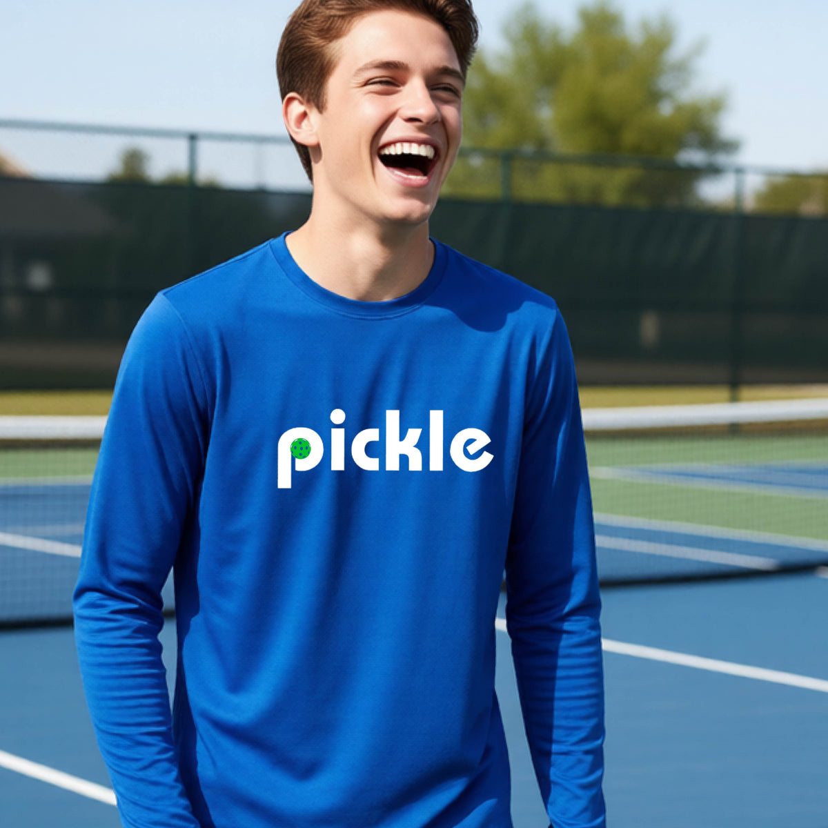 A young person laughing on a pickleball court wearing a royal blue long-sleeve shirt with the word 'pickle' and a pickleball integrated into the P printed across the chest.