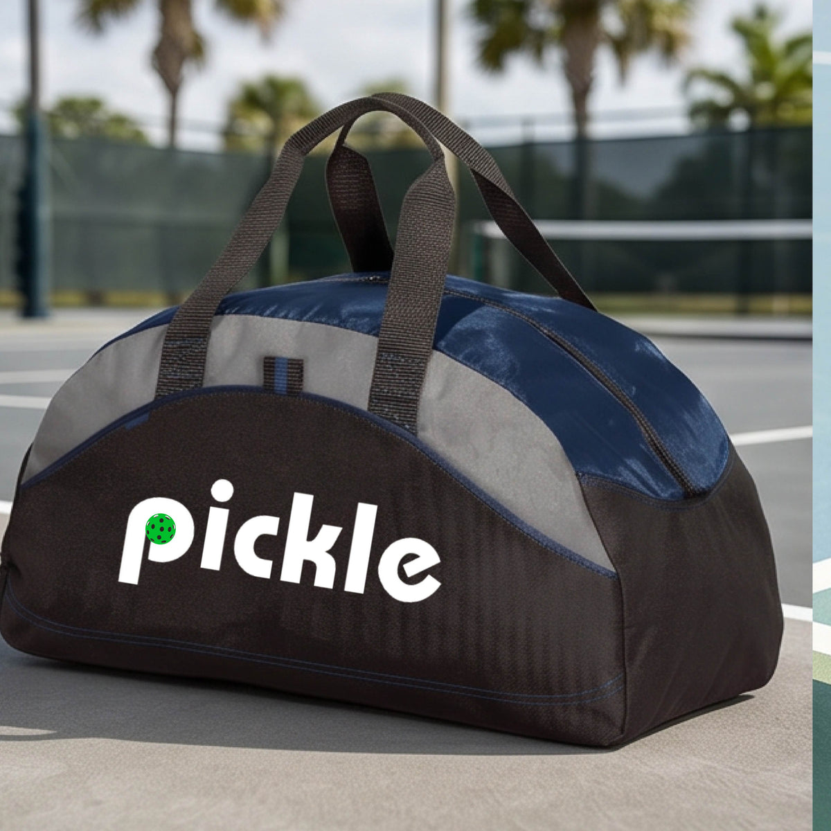 A navy blue, black, and gray duffel bag with the white text  'pickle' printed in white on the front with a green pickleball in the center of hte letter P, placed on a outdoor pickleball court.