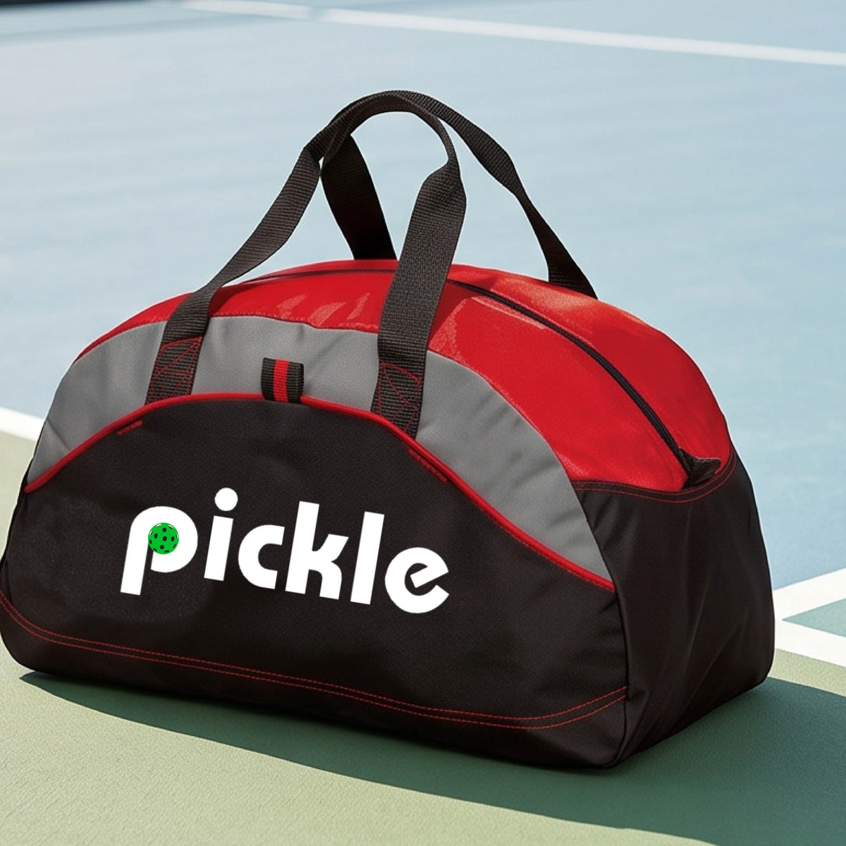 A red, black, and gray duffel bag with the white text  'pickle' printed in white on the front with a green pickleball in the center of hte letter P, placed on a outdoor pickleball court.
