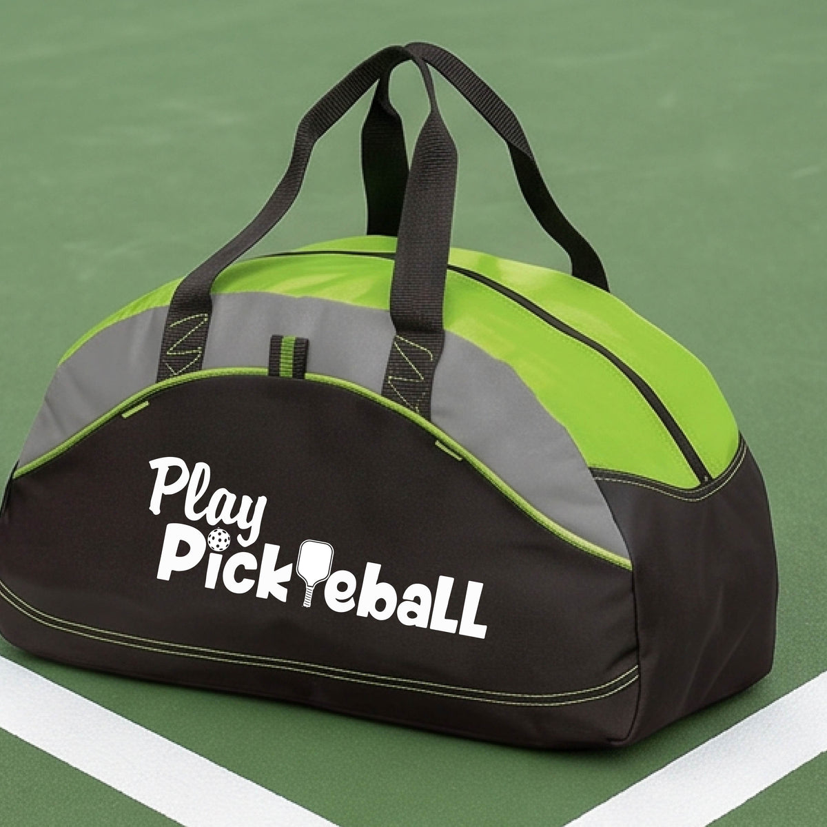 A duffel bag for pickleball on a green picleball court. The bag is black and lime green with gray panels, featuring the text 'Play Pickleball' in white on the front.