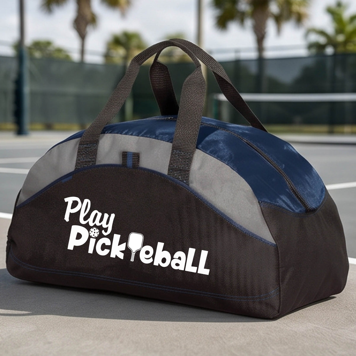 A duffel bag for pickleball on a green picleball court. The bag is navy blue and lime green with gray panels, featuring the text 'Play Pickleball' in white on the front.